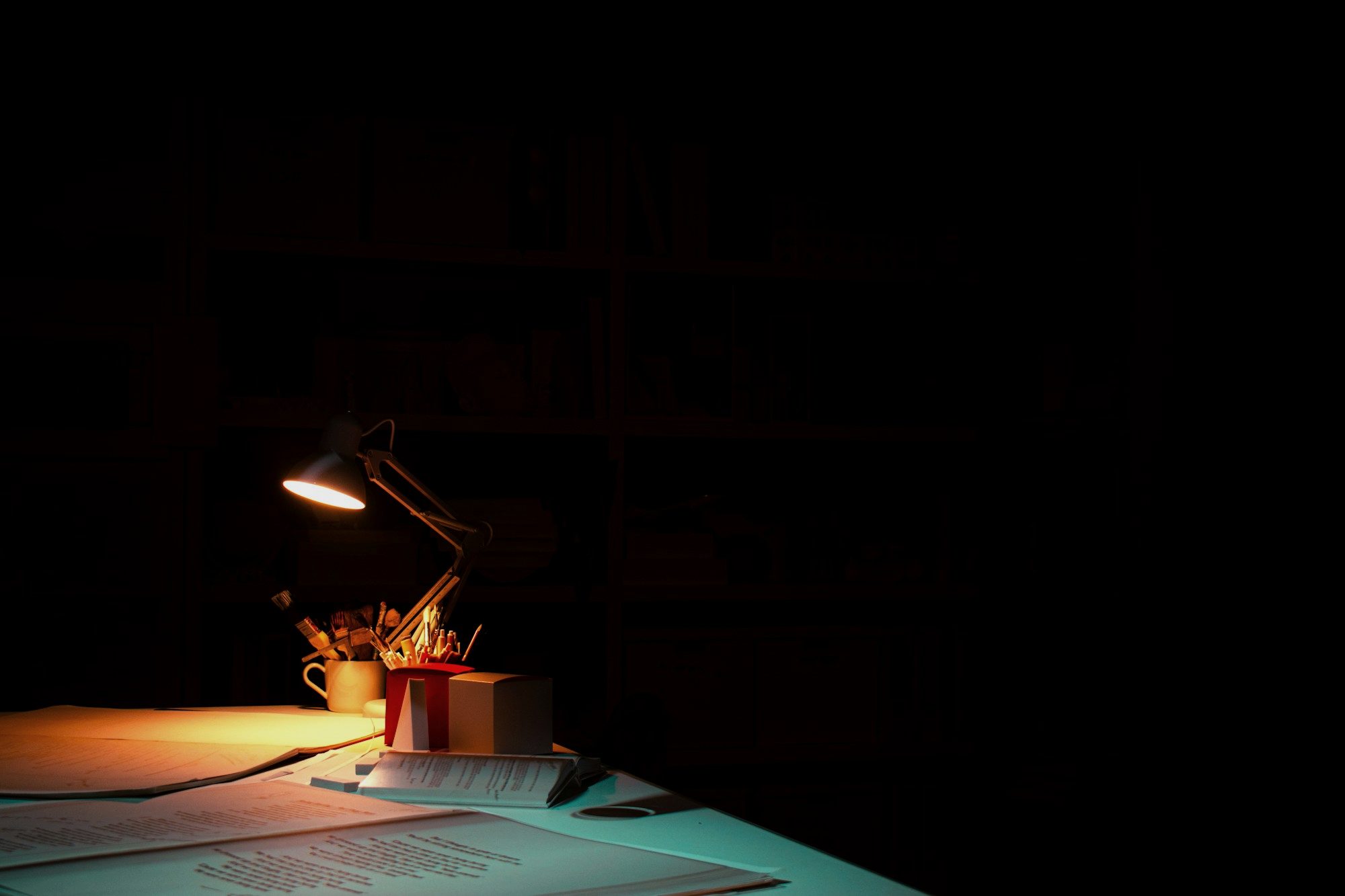 A desk lamp lighting a desk in a dark room
